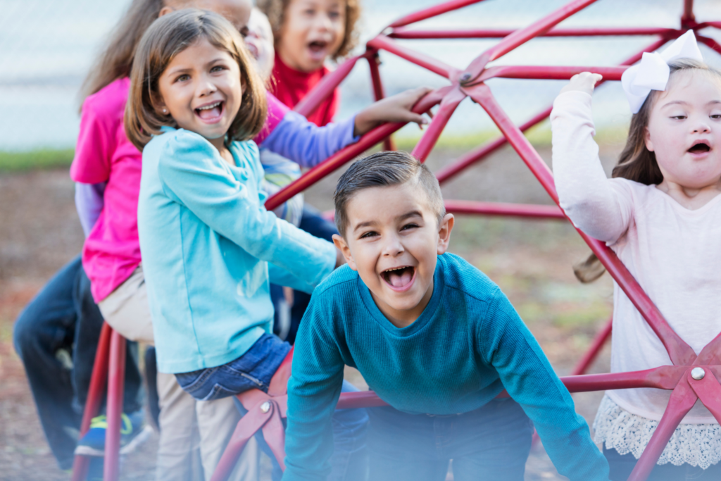 A diverse group of young children, including a child with Down syndrome, playing on a playground geodome