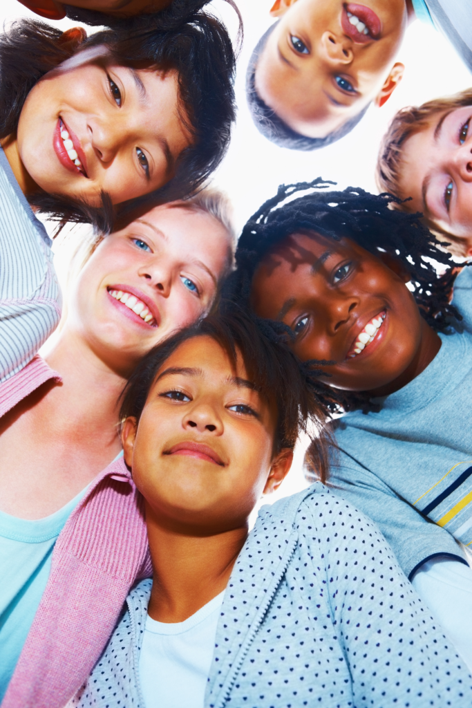 A diverse group of children huddled in a circle, looking down at the camera and smiling