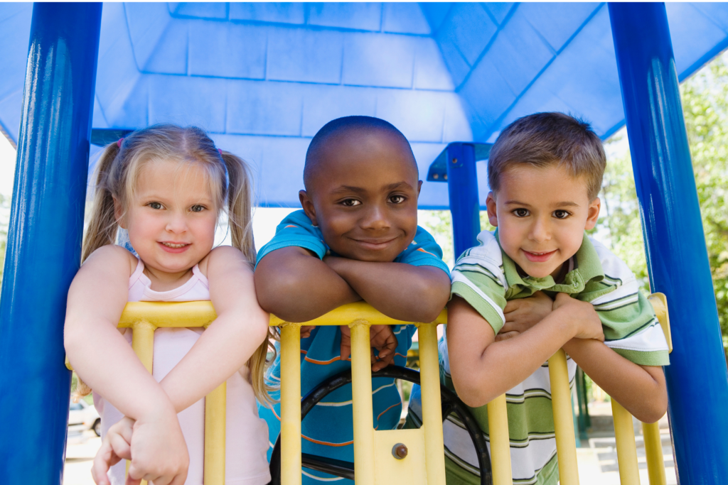 Three young children leaning out of brightly-painted playground equipment, smiling