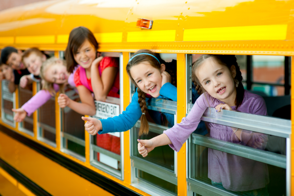 Children waving and smiling out of the windows of a yellow school bus