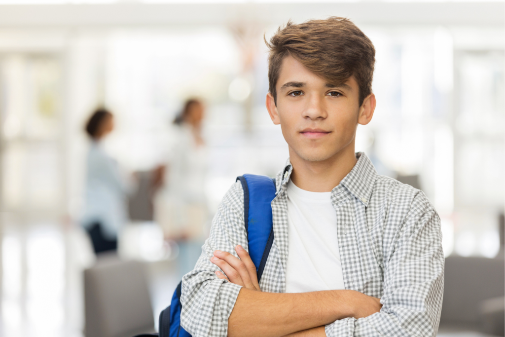A teenager standing confidently with arms crossed, wearing a backpack, in a school setting